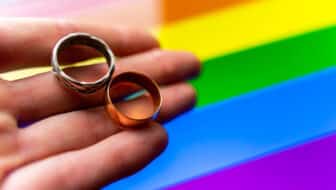 gay wedding proposal. hand holds two wedding rings on lgbt flag background. same-sex marriage, homosexuality and legalized relationship of two lgbt people.
