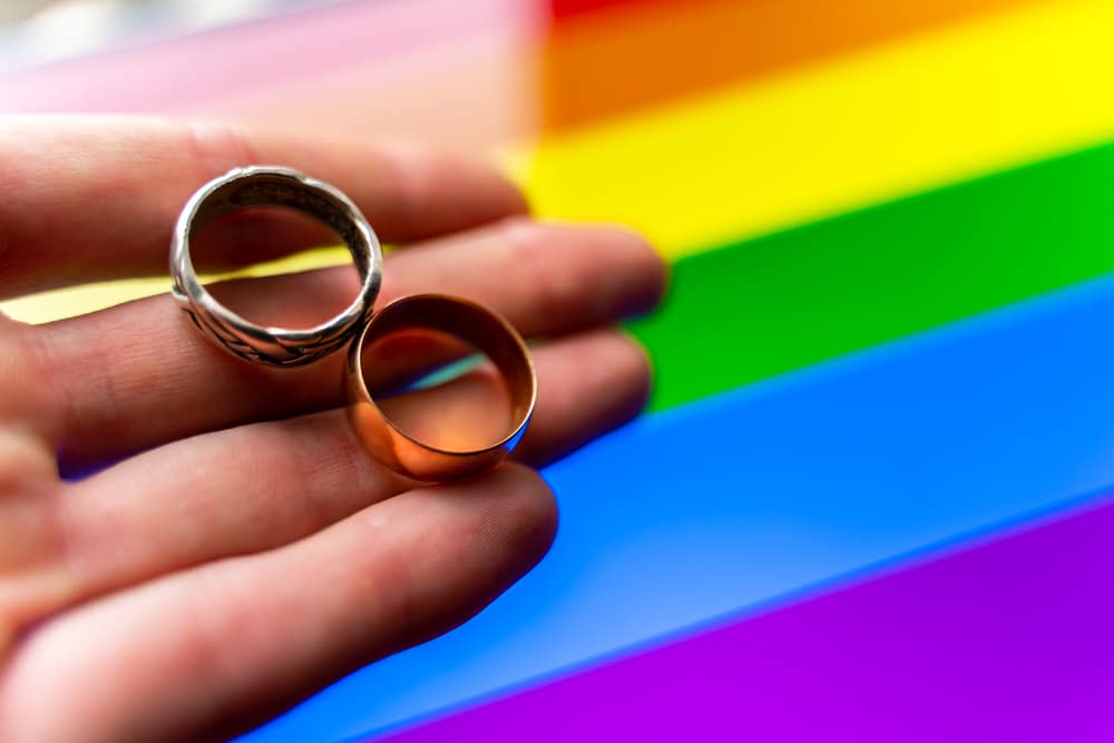 gay wedding proposal. hand holds two wedding rings on lgbt flag background. same-sex marriage, homosexuality and legalized relationship of two lgbt people.